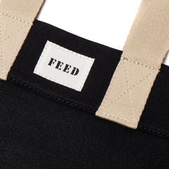 Black | Logo detail of black FEED 10 tote bag with FEED the Children of the World text.